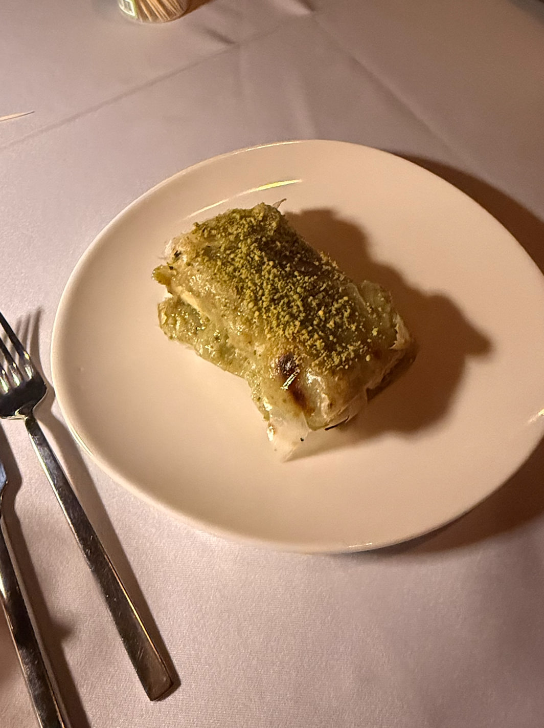 Katmer pastry topped with pistachio on a white plate.